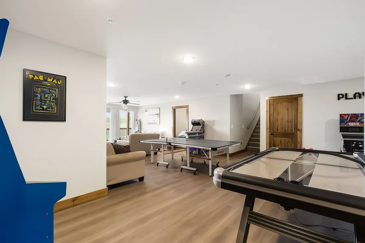 A dynamic entertainment space with an arcade game, ping pong table, air hockey table, and a comfy sofa. The layout invites socializing, gaming, and watching TV, all in one open area designed for fun and bonding.