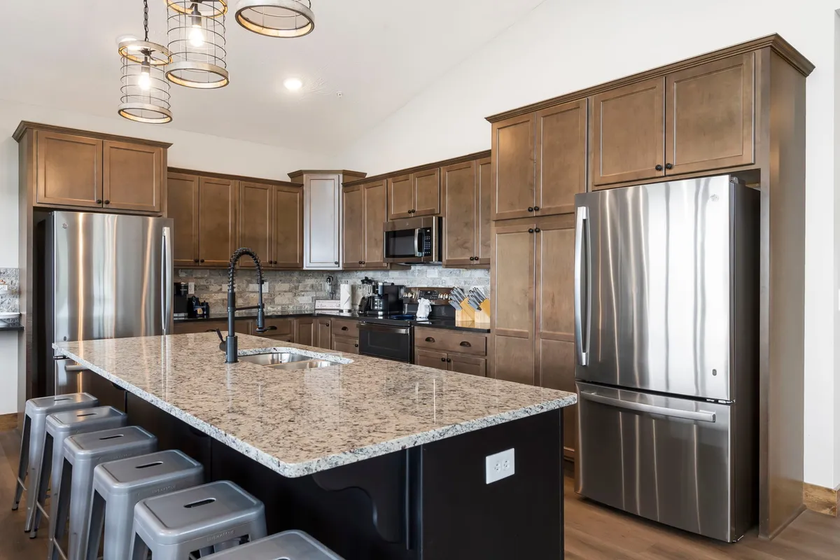 A modern kitchen with a large granite island, stainless steel appliances, and inviting lighting. The setup is ideal for cooking, casual conversations at the bar seating, and entertaining guests.