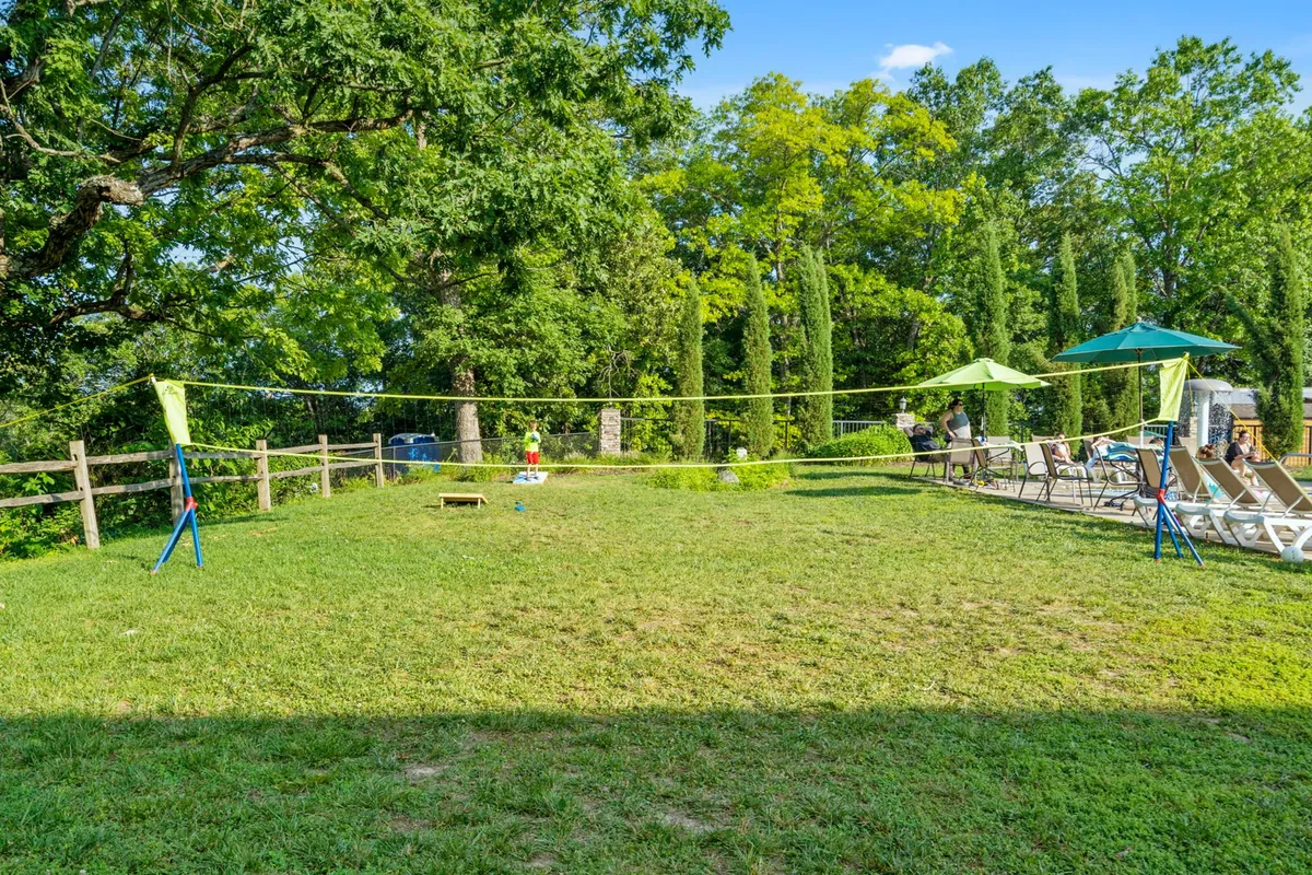 This exterior image features a volleyball net set up on a lawn, surrounded by lounge chairs and umbrellas. Trees provide a lush backdrop, setting the scene for outdoor sports and gatherings.