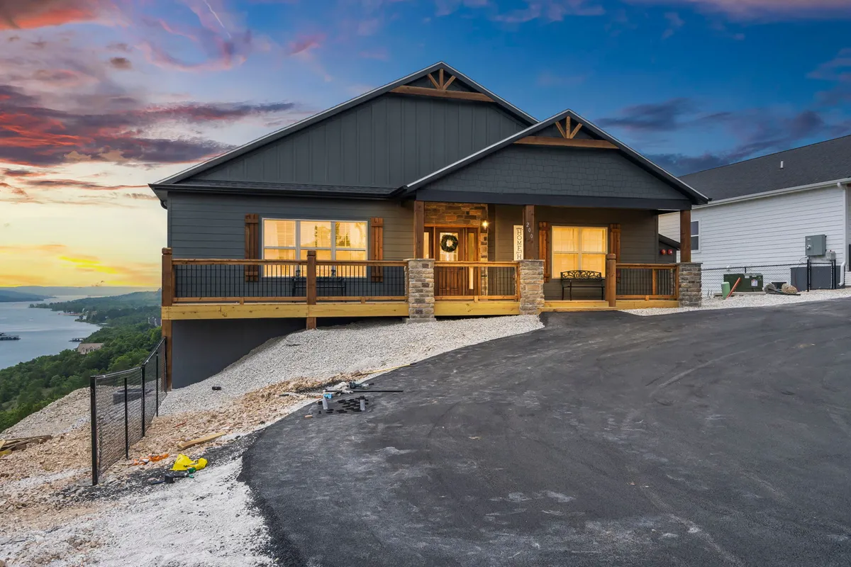 The front porch of the property, featuring large windows, stone accents, and landscaped surroundings. The inviting porch is designed for relaxing and social gatherings with beautiful sunset vistas.