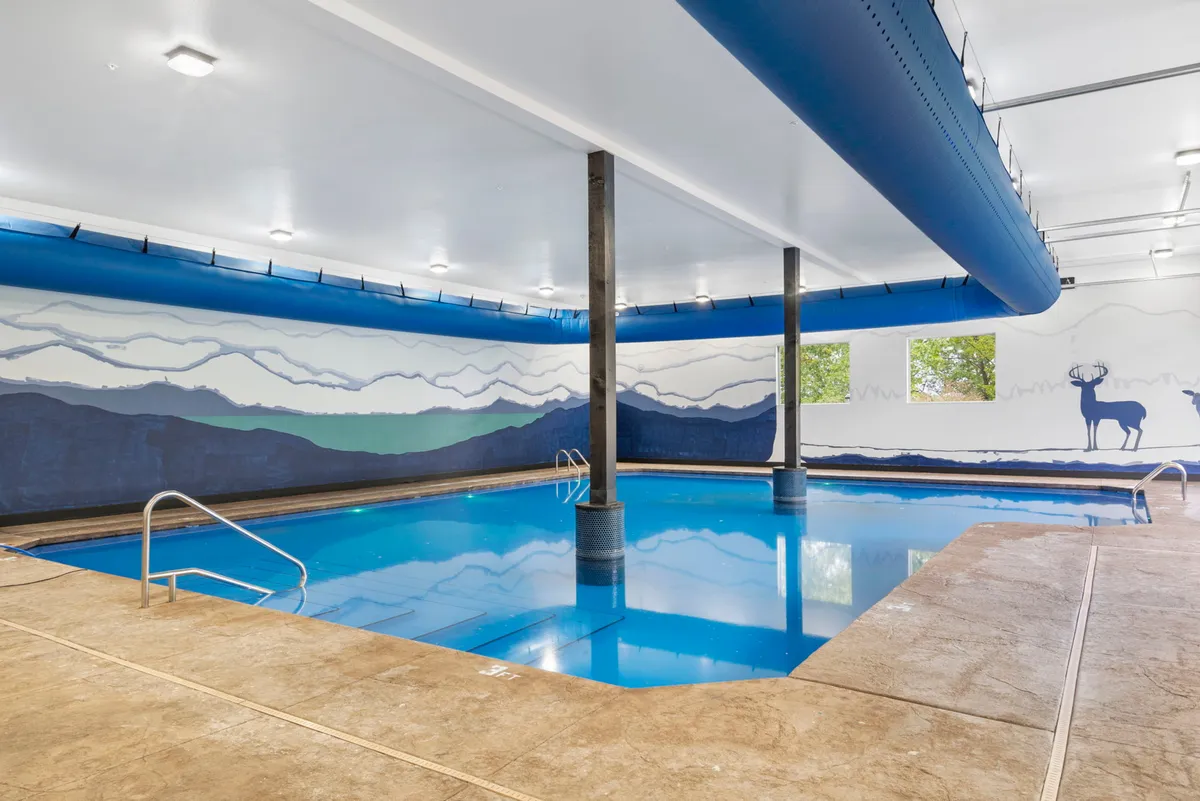 An inviting indoor swimming pool with a scenic mountain mural and expansive windows that flood the space with natural light. The tranquil environment is ideal for year-round relaxation and group gatherings.