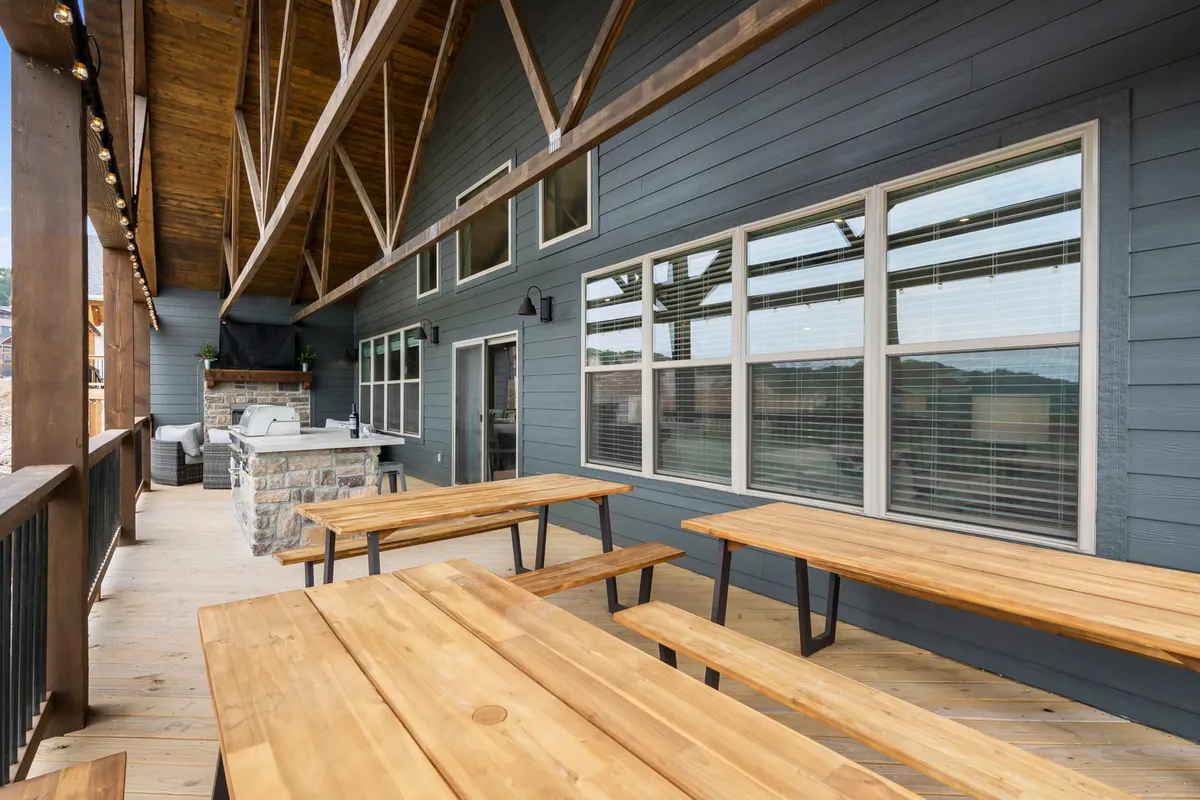The photo features wooden picnic tables and a stone grill area set outside, with large windows providing views into the interior. The mood is casual and relaxed, perfect for outdoor dining, barbecuing, or simply socializing after a hike or bike ride.