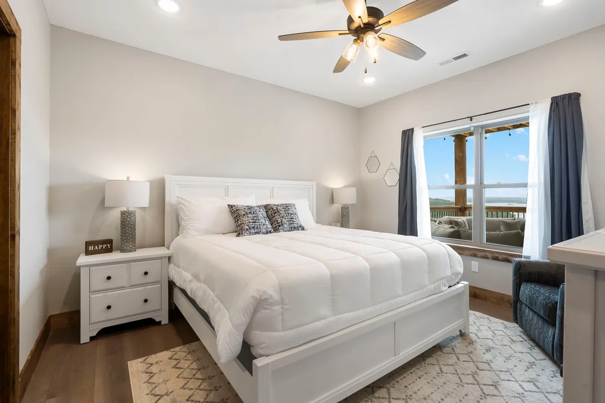 A serene bedroom with a bed positioned next to a window overlooking a scenic view, a nightstand, and a cozy armchair. The natural light and peaceful surroundings create an ideal retreat for relaxation and unwinding.