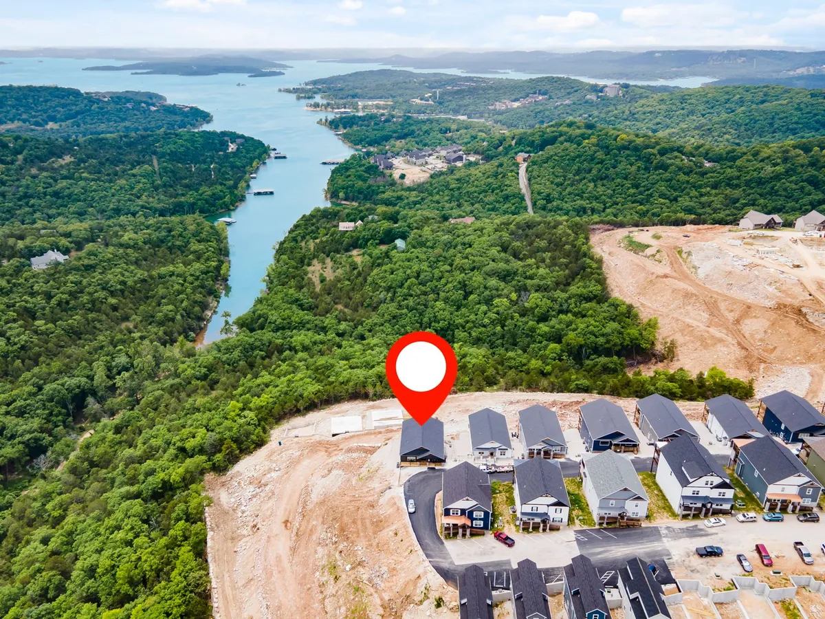 A wide scenic view showing houses nestled along the lake with lush greenery. The image highlights the proximity to the water, boating opportunities, and the tranquil natural environment surrounding the property.