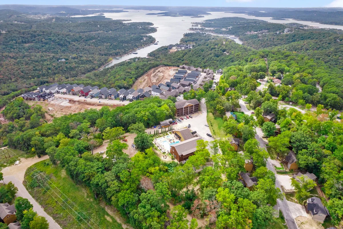 An elevated exterior shot featuring lush greenery, a picturesque lake, and a housing development with a visible swimming pool. The landscape radiates tranquility, while the presence of community spaces highlights recreational opportunities.