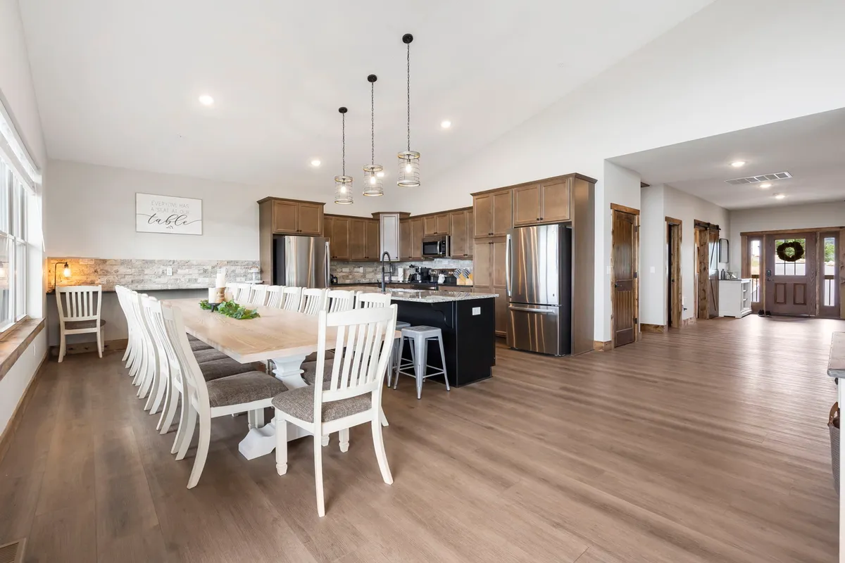 A warm, inviting dining area with a long wooden dining table and an adjacent kitchen island, complemented by stylish cabinetry and hanging lights. The layout is perfect for large groups, communal meals, and festive occasions.