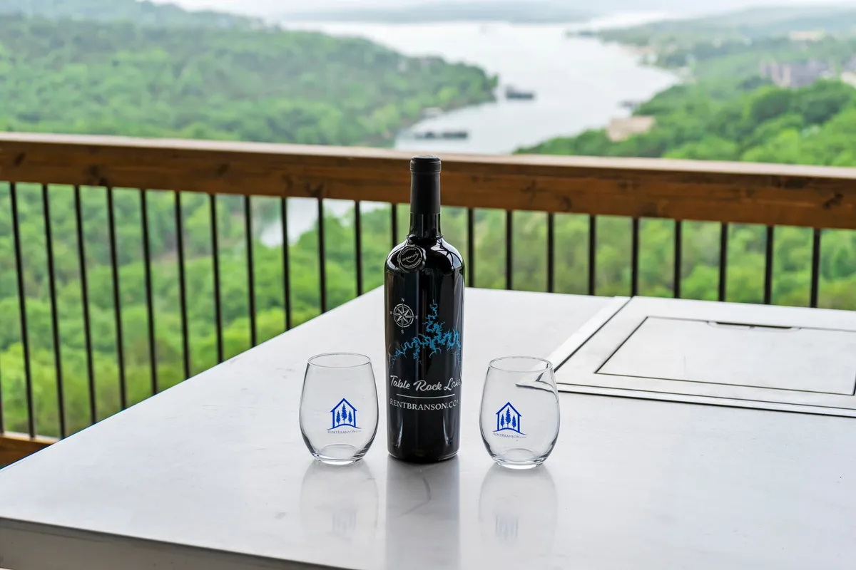 A bottle of wine and two glasses are set on an outdoor table with a scenic view stretching into the distance. The composition conveys relaxation, a leisurely pace, and an appreciation of nature’s beauty, ideal for peaceful moments following more active adventures.