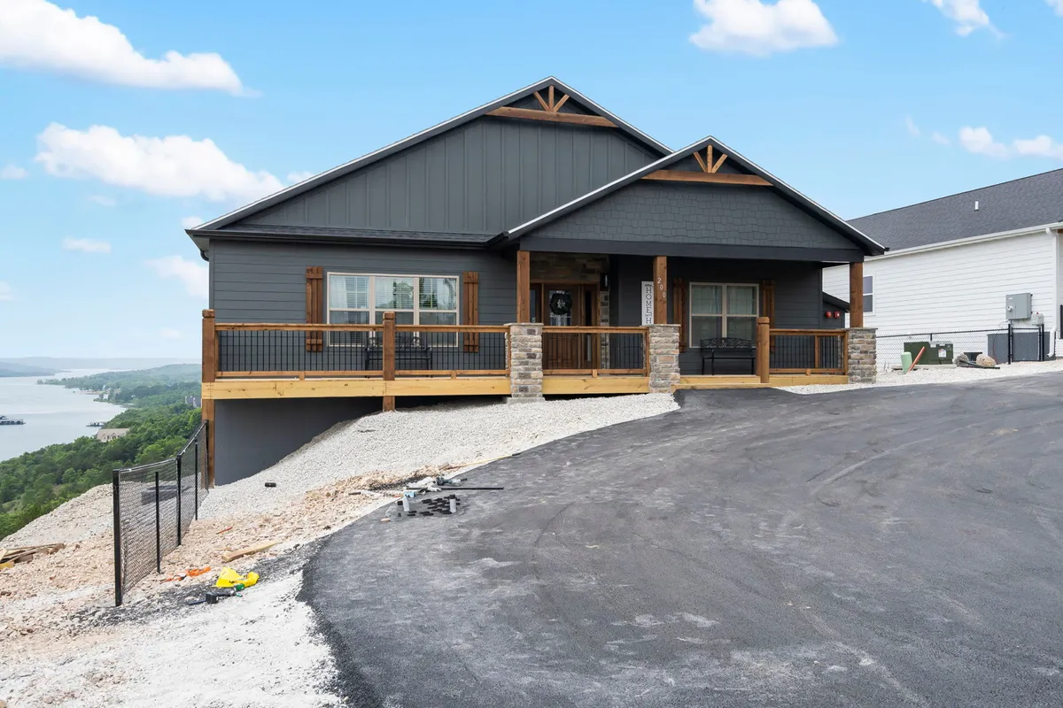 This exterior shot captures the home's front porch, stone pillars, and large windows, with a deck overlooking the water. The visible seating areas and expansive view highlight the direct connection to Table Rock Lake and provide a sense of tranquility and welcome. The deck is perfectly positioned for watching sunrises and sunsets—ideal for memorable group photos, as described in the section.